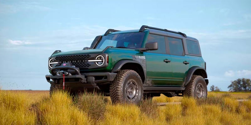 Front view of a green 2024 Ford Bronco SUV parked in a grassy field under a blue sky