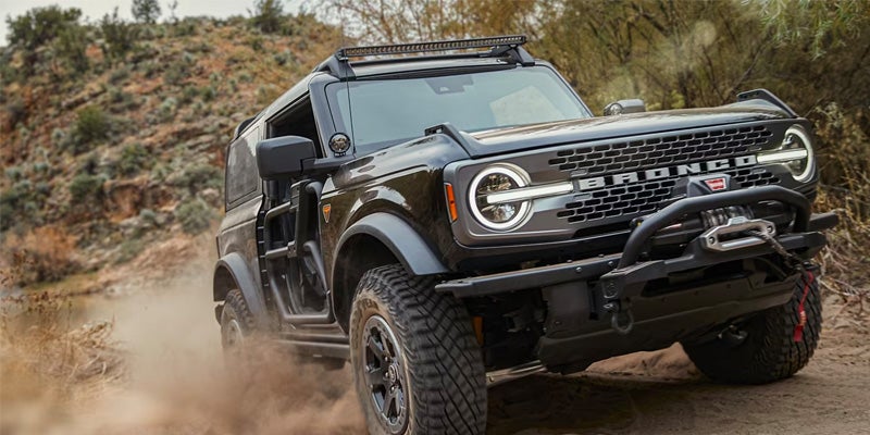 Black 2024 Ford Bronco driving off-road with doors removed, kicking up dirt
