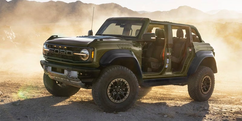 A 2024 green Ford Bronco off-road vehicle with doors removed, parked on a desert terrain with mountains in the background