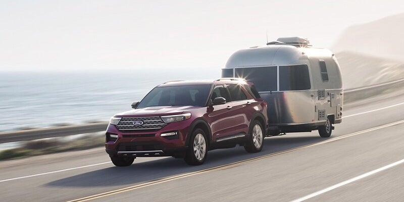 A red 2024 Ford Explorer driving on a public road with a camper hooked up