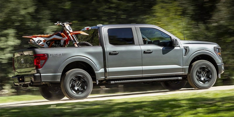 The 2024 Ford F-150, with a dirt back on the truck bed, driving on a highway