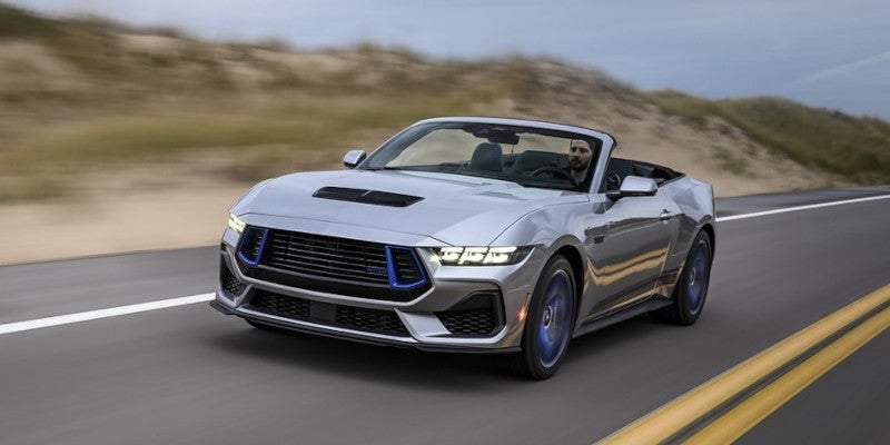 The front-side view of a 2024 Ford Mustang driving on a highway